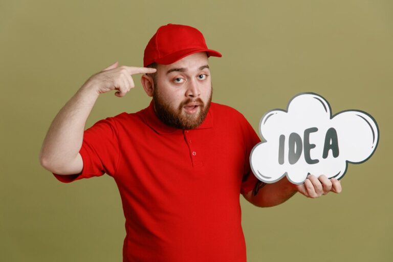 delivery-man-employee-red-cap-blank-tshirt-uniform-holding-bubble-speech-with-word-idea-looking-camera-pointing-with-index-finger-his-head-standing-green-background_141793-134926 (1)